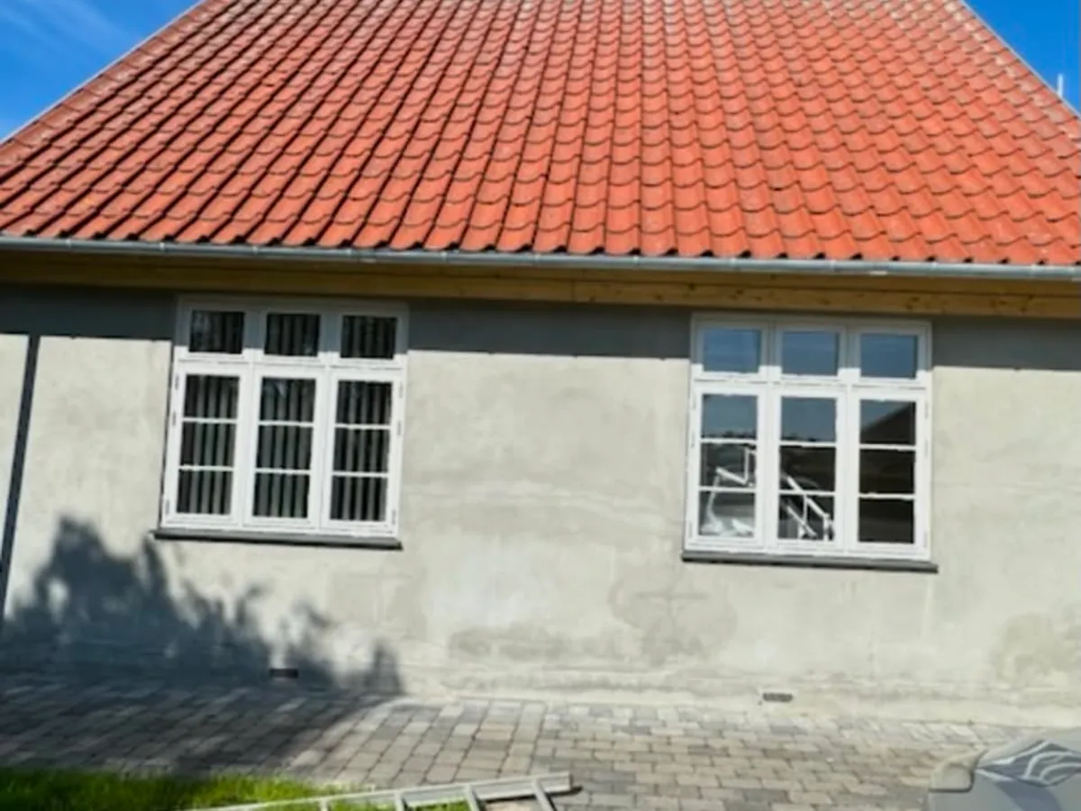 Enfamiliehus med rødt tegltag og skjoldet, gråt puds før facademalingen
