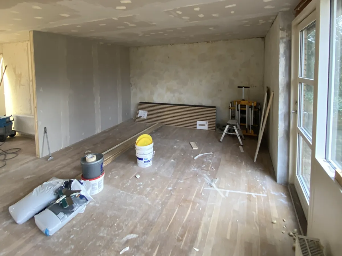 Stue under renovering med spartlede gipsvægge og afdækket gulv